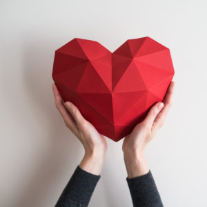 Two female hands holding red polygonal paper heart shape