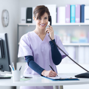 Happy woman in a medical office wearing scrubs and talking on the phone