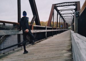 man jogging and stretching over a bridge to promote health
