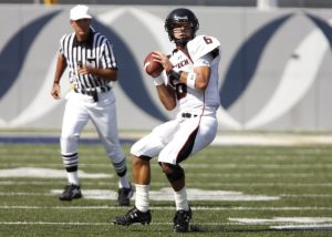 Football player getting ready to throw the football on the field with a referee behind him