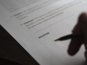 Close-up visual of a person holding a pen to an important legal document near the signature area