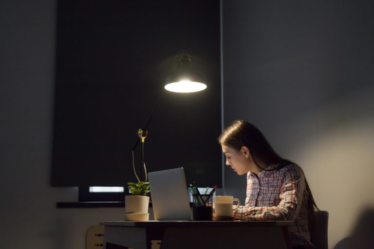 A woman sitting alone at in a small room with her laptop open to study