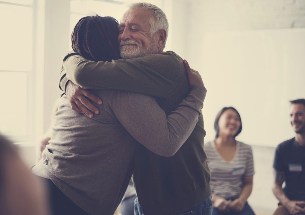 Man in group therapy hugging a woman in comfort