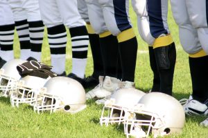 Student athlete football players standing in a line on a football field with their helmets by their feet