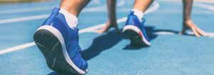 Sprinter waiting for start of race on running tracks at outdoor stadium. Sport and fitness runner man athlete on blue run track with running shoes. Banner panorama.