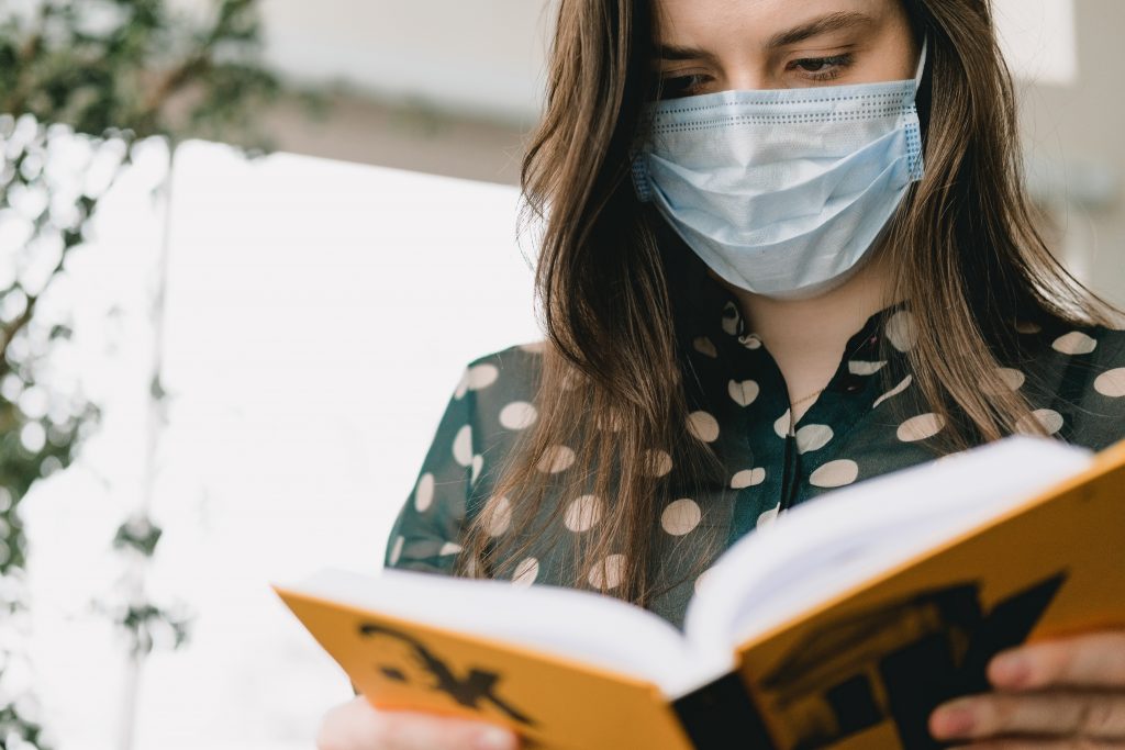 Girl student reading a book while wearing a protective mask