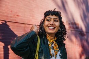 Young, eclectic, latina college student smiling on campus against a brick wall