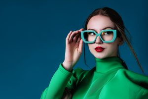 A portrait of an attractive young woman wearing green beautiful dress, one hand holding the green eye glasses