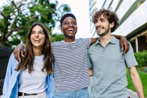 Happy multi-ethnic group of best millennial friends hugging each other laughing together walking outdoor. Unity people and friendship concept
