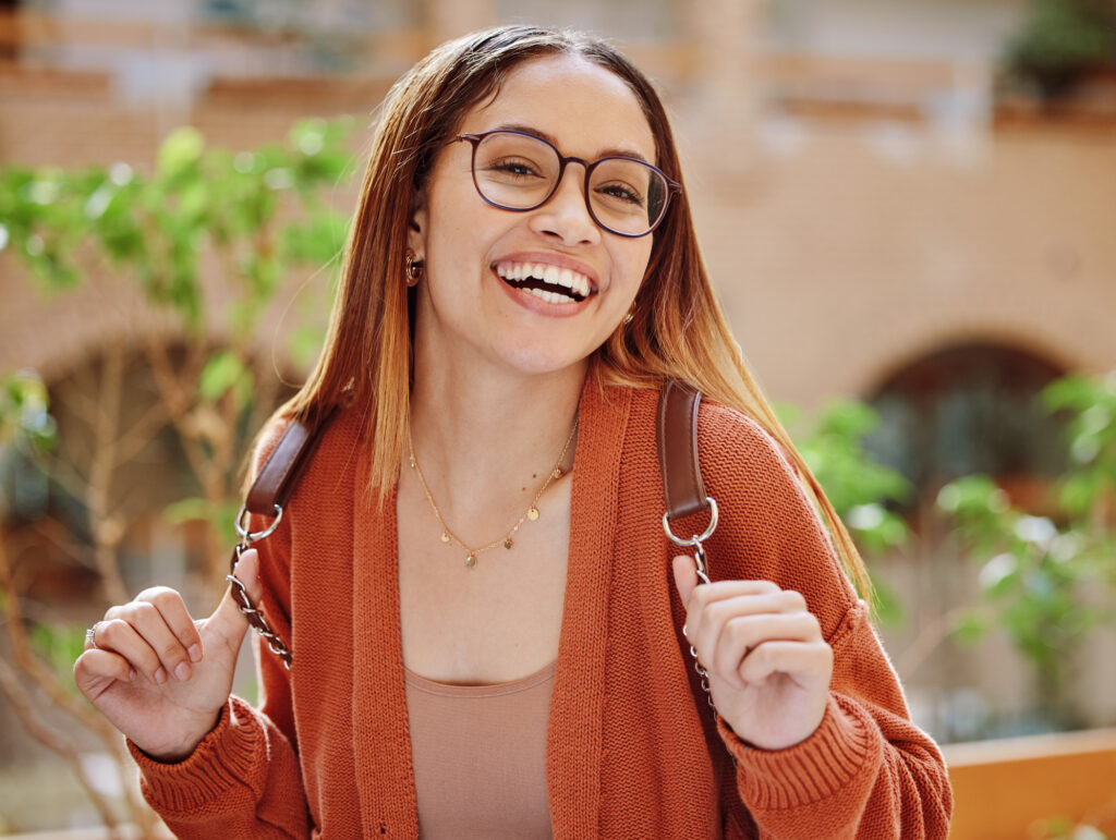 Happy female college student with glasses smiling on campus in an orange cardigan