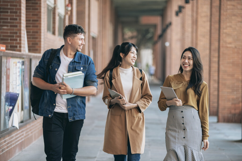 three international students dressed well and walking to class with books in hand